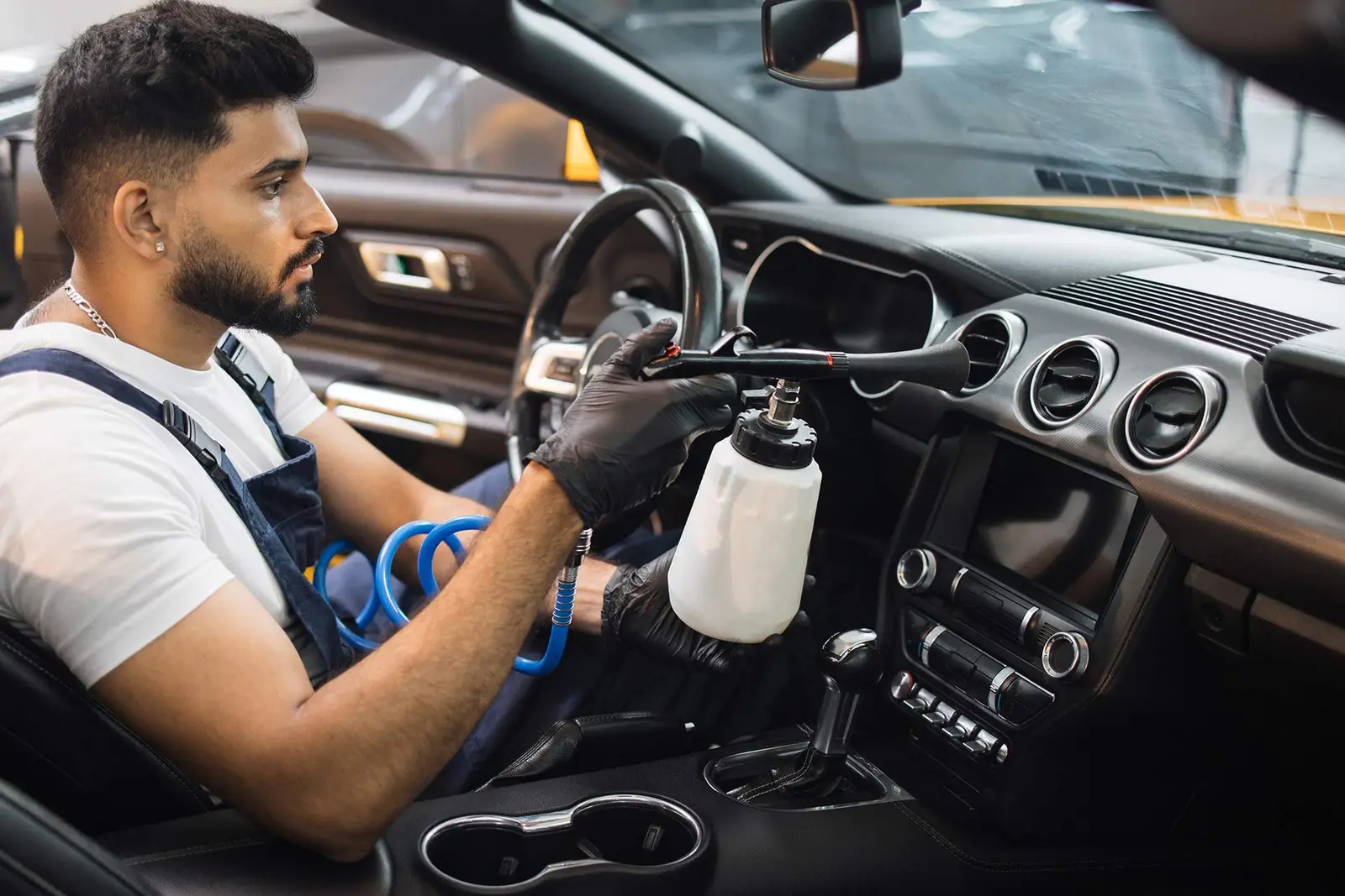 Professional detailer cleaning car interior with spray equipment